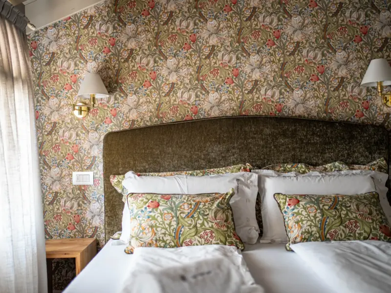 Letto matrimoniale con testata in velluto verde oliva, cuscini decorativi a motivo floreale, applique e tende chiare